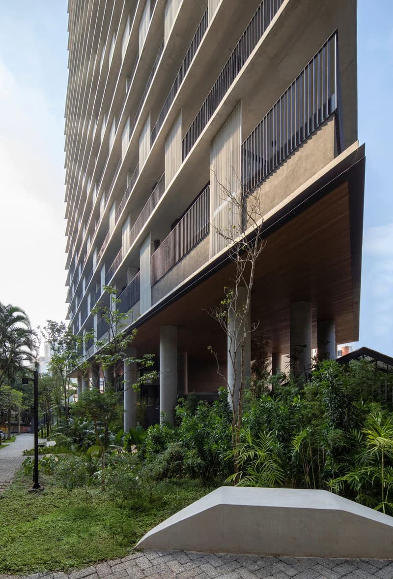Deep planted ground-level space beneath the residential floors and balconies of Onze22 in São Paulo.