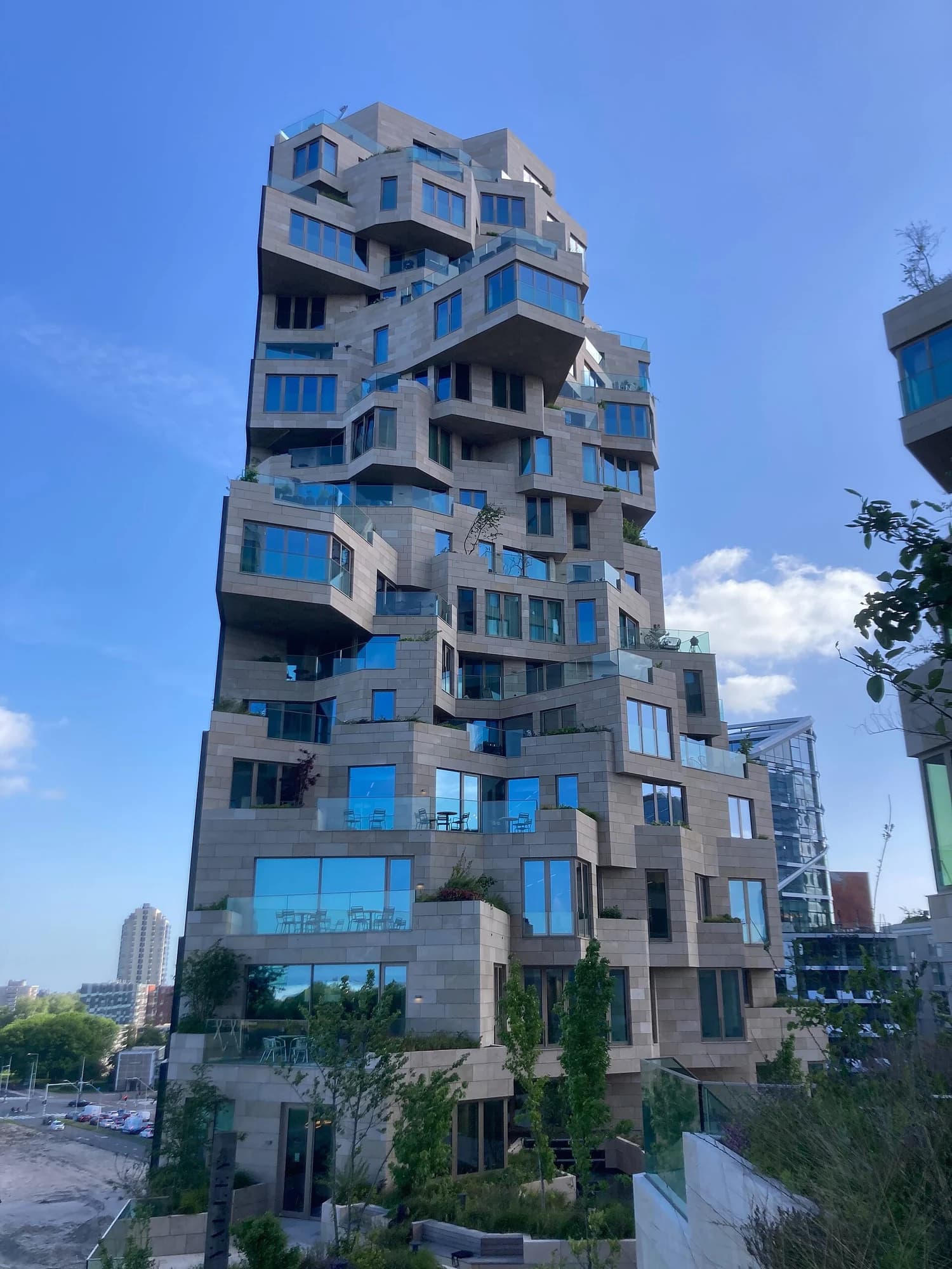 A planted residential tower at Valley in Amsterdam, with projecting stone-faced terraces against blue sky.