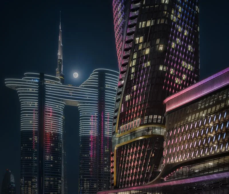 Wasl Tower illuminated beside the Burj Khalifa at night · Ahmad Alnaji - SARAB · via v2com